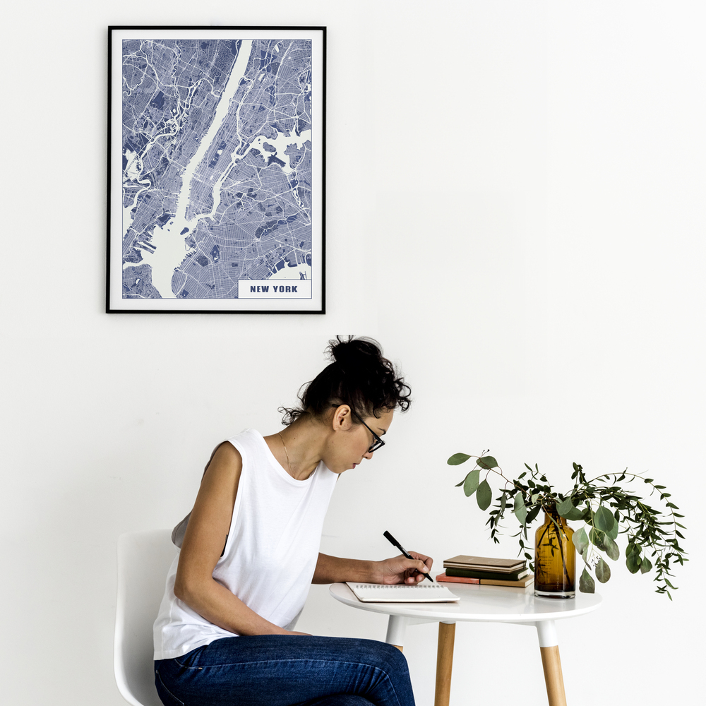 Póster del plano de Nueva York en azul y blanco, con marco negro en una pared blanca sobre una mesa redonda