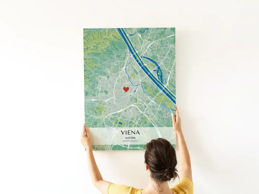 Póster de mapa urbano en verde y azul con corazón y coordenadas en una franja clara, sobre una pared blanca