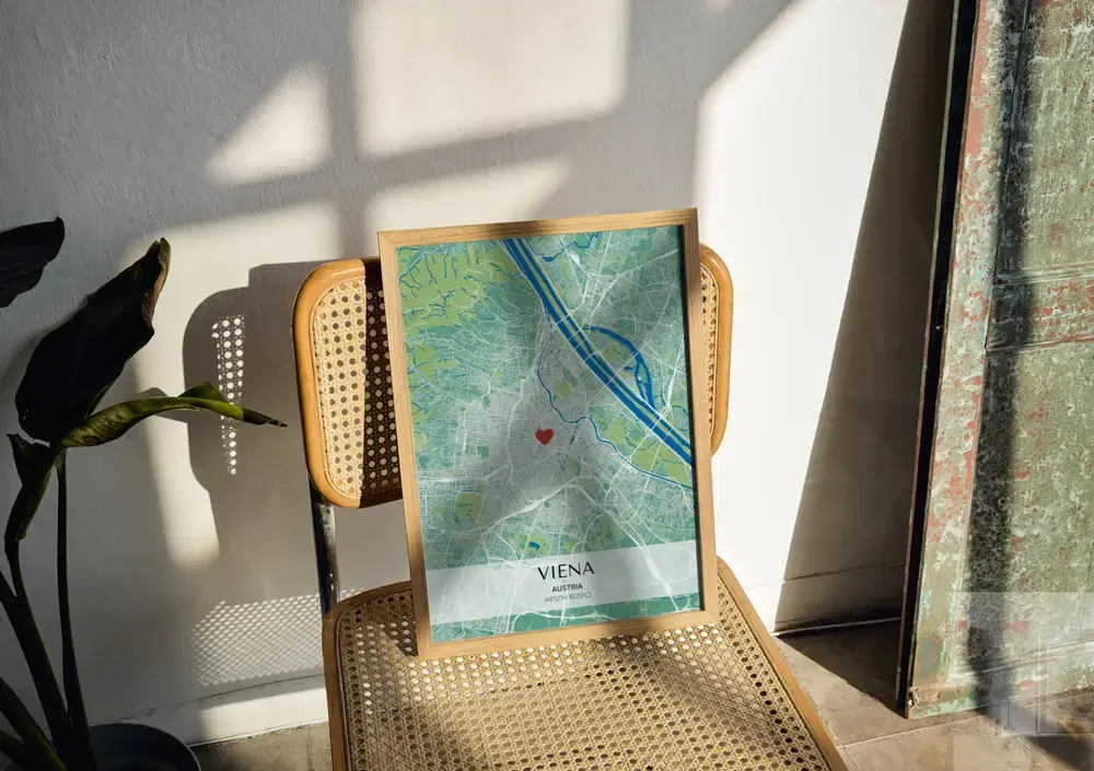 Póster de mapa urbano en verde y azul con coordenadas, en marco de madera sobre una silla de rejilla al sol